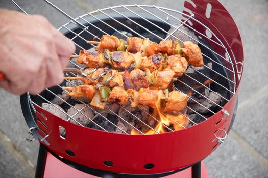 man flipping chicken skewers on barbecue grill over hot coals, summer delicacies, vacation food on terrace. High quality photo