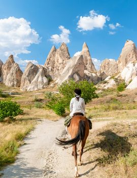 young woman during a vacation in Turkey Kapadokya watching the hot air balloons of Cappadocia. Asian women on the back of a brown horse in the valley of Cappadocia