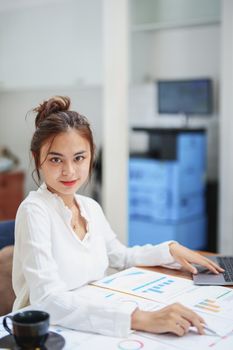 Portrait of a beautiful female employee holding a pen, using a computer and checking the company's budget documents