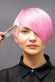 The female hairdresser is combing the dyed pink short hair of the young woman against the dark wall