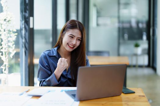 Portrait of an Asian female employee using computer with a smiling face as she works the next morning.