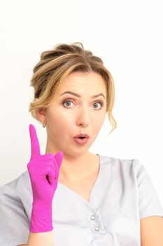 Young caucasian woman doctor wearing pink gloves keeping index finger pointed upwards making a gesture with index finger. I have an idea