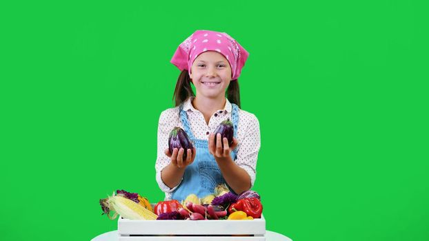 cute, smiling, little farmer girl shows a box with different fresh vegetables, harvest. on green background in studio. Healthy food to your table, Healthy nutrition. High quality photo