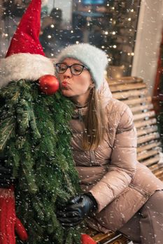 Pretty woman kissing tree decorated mannequin. Xmas holidays, New Year or Christmas concept