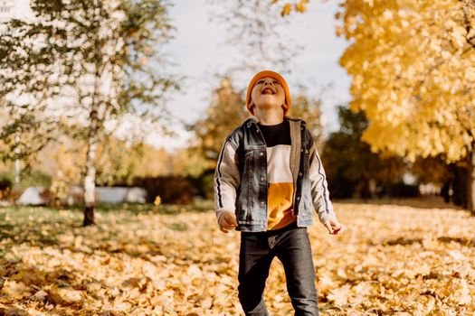 Kid having fun in autumn park with fallen leaves, throwing up leaf. Child boy outdoors playing with maple leaves