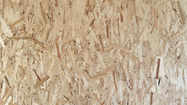 OSB boards are made of brown wood chips sanded into a wooden background. Top view of OSB wood veneer background, tight, seamless surfaces.