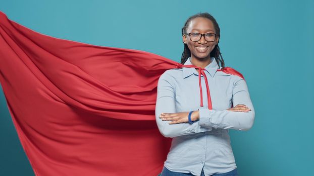 African american woman posing as superhero with red flying cape, wearing cartoon comic costume with cloak on camera. Feeling confident and powerful as hero, strong action character.