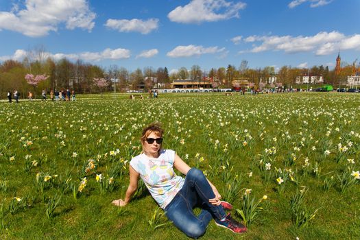 Happy young woman sitting in city park planted with daffodils.