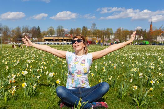 Happy young woman sitting in city park planted with daffodils.