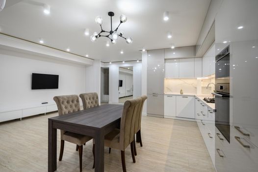 Interior of a huge white luxury kitchen in a studio apartment, lots of copy space, closeup view to dining table with chairs