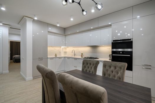 Interior of a huge white luxury kitchen in a studio apartment, lots of copy space, closeup view to dining table with chairs