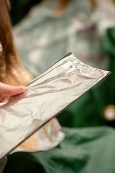 Hairdresser's Hands Holding Foil Sheet For Hair Dye In Beauty Salon