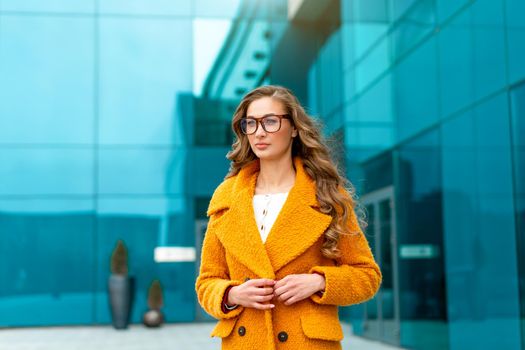 Business woman dressed yellow coat standing outdoors corporative building background Caucasian female business person eyeglasses on city street near office building big windows Stylish businesswoman