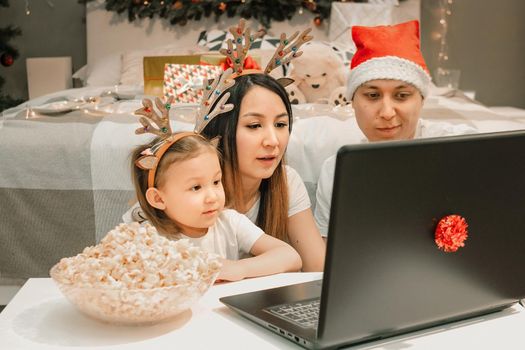 Cozy family christmas with father mother and child girl daughter, watching video on laptop in bedroom, happy fun and xmas holiday together at movie night or via video link, authentic festive lifestyle