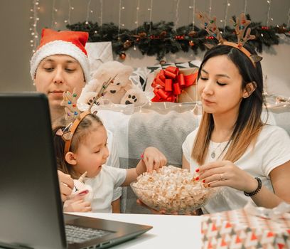 Cozy family christmas with father mother and child girl daughter, watching video on laptop in bedroom, happy fun and xmas holiday together at movie night or via video link, authentic festive lifestyle