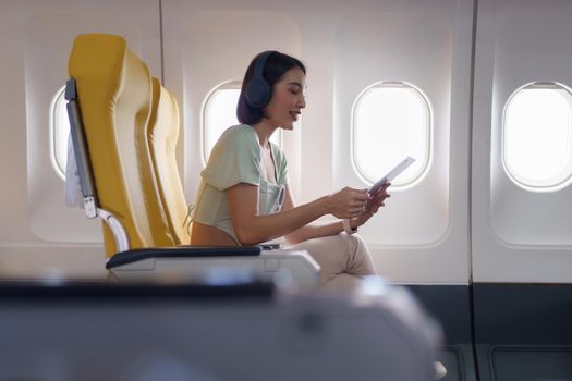 Young asian woman using digital tablet connected to wifi internet during flight on board. Travel concept.