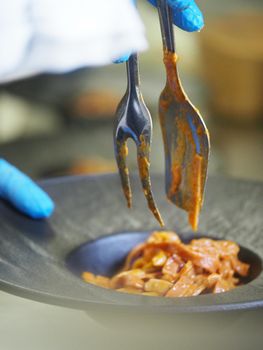 closeup of a chef hand wearing gloves serving and decorating a plate of pasta