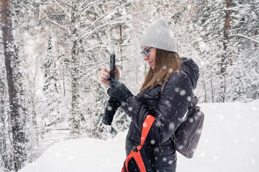 Woman taking photo on phone in snowy winter forest, snowy winter day