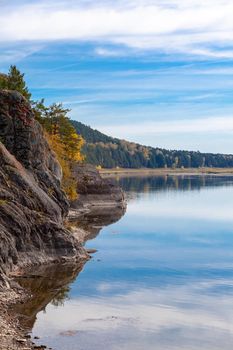 Beautiful, wide autumn river among forests and rocky shore. A calm and quiet place with autumn colors. Reflection of clouds in the water in good weather