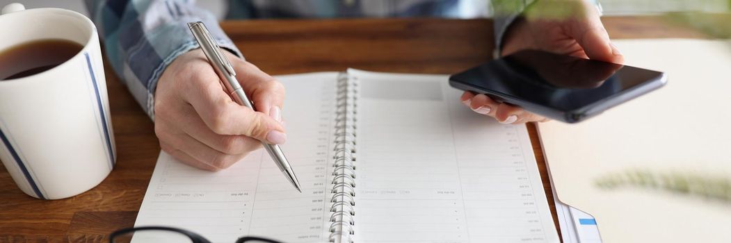 Close-up of person start day right with planner and cup of coffee, make appointment, plan. Journal, diary, creativity, writer, workplace, set goal concept