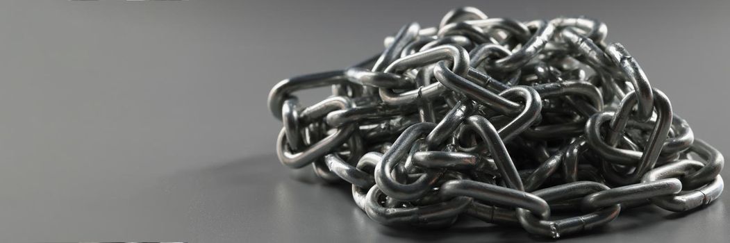 Close-up of grey chain folded in heap, steel metal iron chain on grey surface. Solid chain tangled in mess. Locking equipment, fixation instrument concept