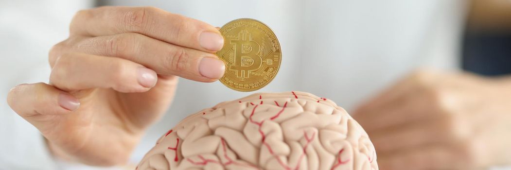 Close-up of businesswoman holding bitcoin coin in front of human brain. Smart part of human body, create idea, find ways to earn. Intellect, invest concept