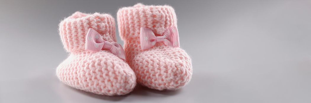 Close-up of pair of knitted pink baby booties with cute bow on it. Handicraft shoes for newborn baby on grey surface. Handmade, crochet, wool, care concept