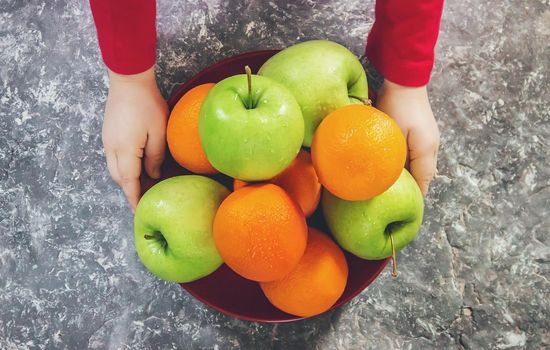 apples and oranges in the hands of a child.