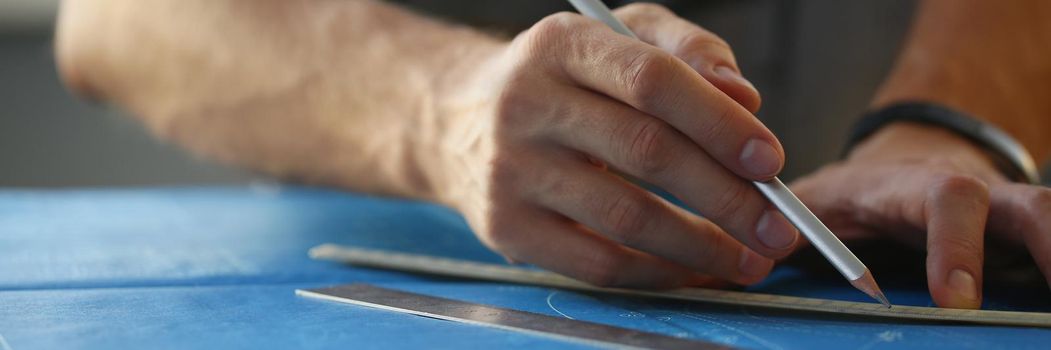 Close-up of builder man hand holding pencil and make corrections on building plan. Engineering blueprint design for buildings on desk. Architecture concept