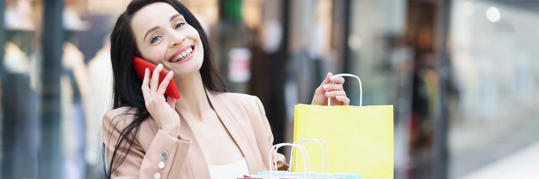 Portrait of female shopaholic talk to friend on smartphone sitting outside with packages. Bunch of colourful packages. Sale, shopping, discount concept