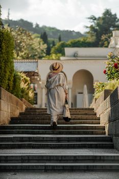 Woman on the stairs in the park. A middle-aged lady in a hat in a white outfit with a bag walks around the Livadia Palace.