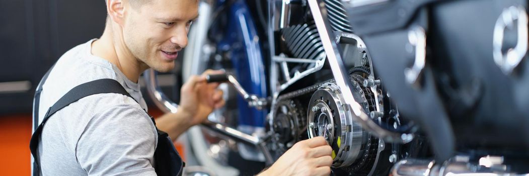 Portrait of qualified handyman with tool fix damaged motorbike in garage. Professional mechanic in uniform, repair and fix. Pit stop, service help concept