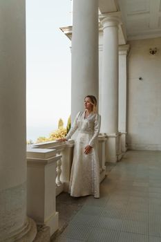 a beautiful mature woman in a long white dress stands on the balcony and looks into the distance.