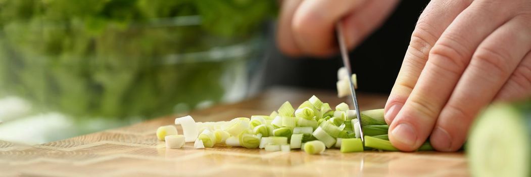 Close-up of professional chef cut spring onion with sharp knife on cutting board. Person follow delicious new recipe. Cooking, food, meal, homemade concept