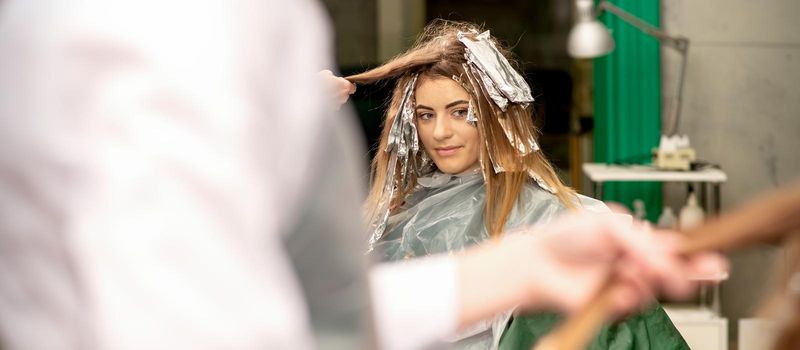 Portrait of a beautiful young caucasian woman who is smiling getting dyeing her hair with foil in a beauty salon