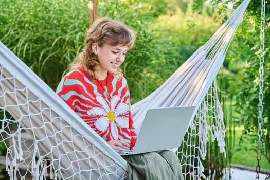 Teenage girl relaxing in hammock using laptop for leisure study. Adolescence, students, high school, technology, lifestyle, youth concept