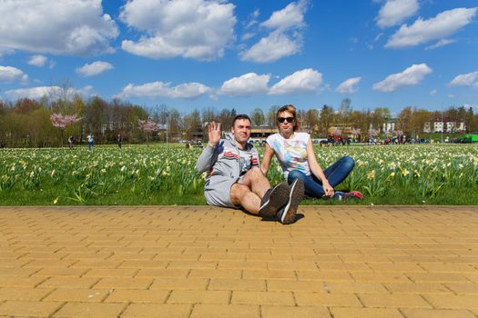 Happy young couple sitting in city park planted with daffodils.
