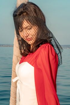 Attractive middle-aged woman in a red dress on a yacht on a summer day. Luxury summer adventure, outdoor activities