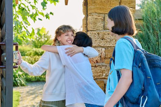 Meeting of friends, young female with guy and girl joyfully hugging near front door to yard. Welcome, youth, friendship, students, lifestyle concept