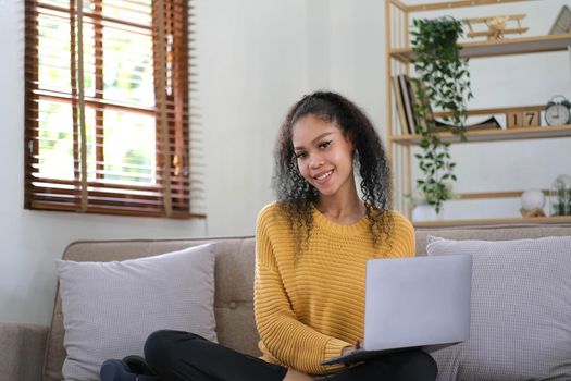 Beautiful Asian woman using digital tablet while headphones sitting on sofa at home.