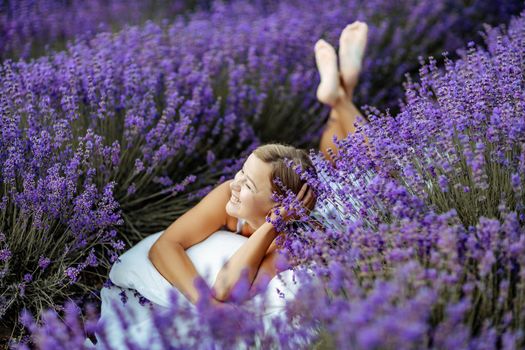 A middle-aged woman lies in a lavender field and enjoys aromatherapy. Aromatherapy concept, lavender oil, photo session in lavender.