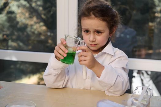 Caucasian little girl in white lab coat, conducts chemical experiment, watching a reactivity taking place in test tube with citric acid and soda, in the school chemistry laboratory. Volcanic eruption