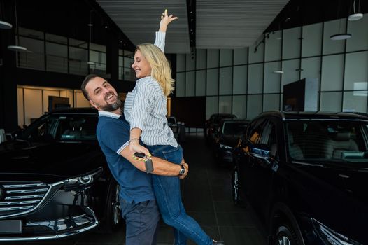 Happy caucasian couple hugging while buying a new car in a car dealership