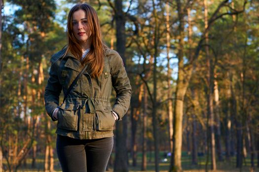 an adult female human being. Lovely young woman in a green jacket in autumn park with pine