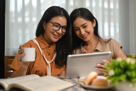 Two cheerful female students are searching online information on digital tablet for their research. Education and Technology concept.