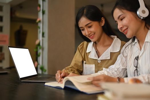 Two young asian woman doing class assignment together and using laptop computer at campus building.