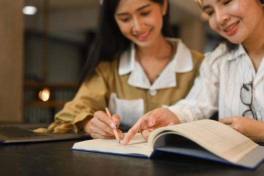 Two smiling college students preparing for exams, learning together in library. Education, people and technology concept.