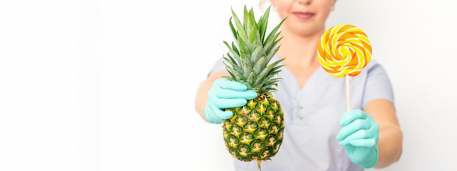 Young caucasian female doctor nutritionist holding fresh pineapple with lollipop over white background