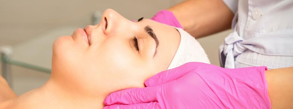 Cosmetologist with gloved hands applies a moisturizing mask with peeling cream on the female face. Facial cosmetology treatment. Procedures for facial care