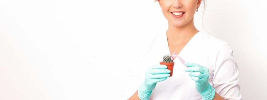 A smiling female beautician holds little green cactus with the razor in her hands. Hair removal concept